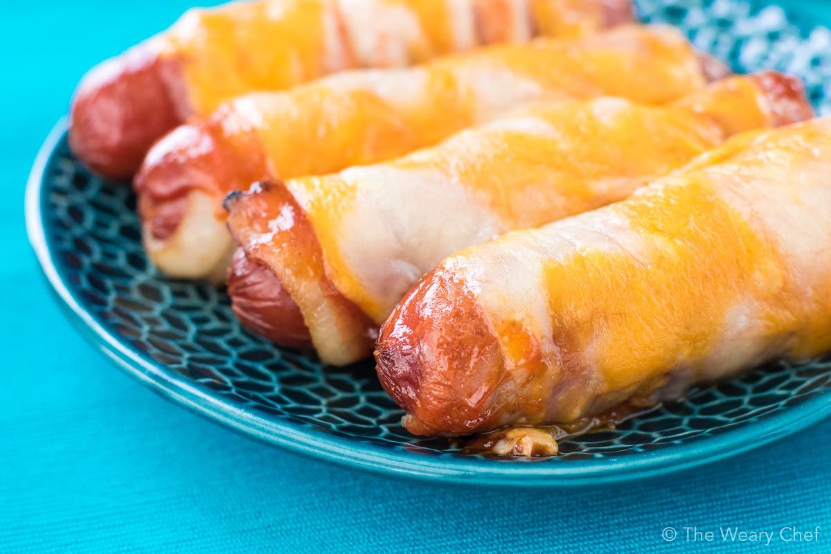 These cheesy BBQ Bacon Wrapped Hot Dogs are fun and easy to make. Perfect for the oven or grill. Serve them on buns or on their own for a lower carb treat!