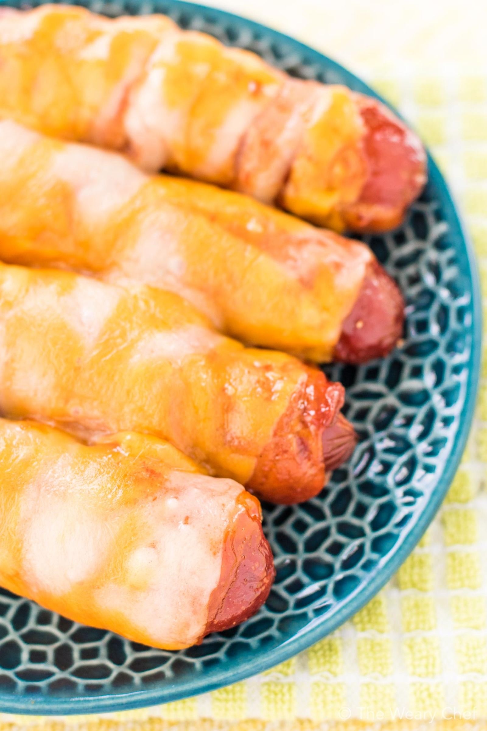 These cheesy BBQ Bacon Wrapped Hot Dogs are fun and easy to make. Perfect for the oven or grill. Serve them on buns or on their own for a lower carb treat!